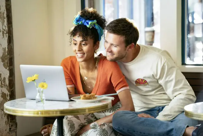 A dating couple sits together looking on a laptop.