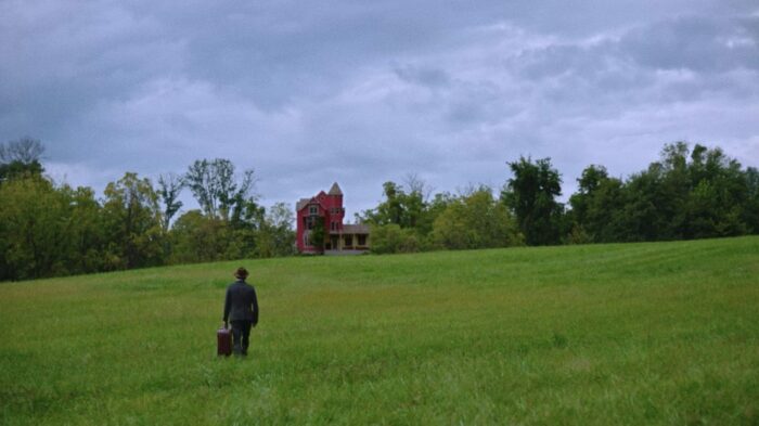 A man walks up a hill to a red country house.