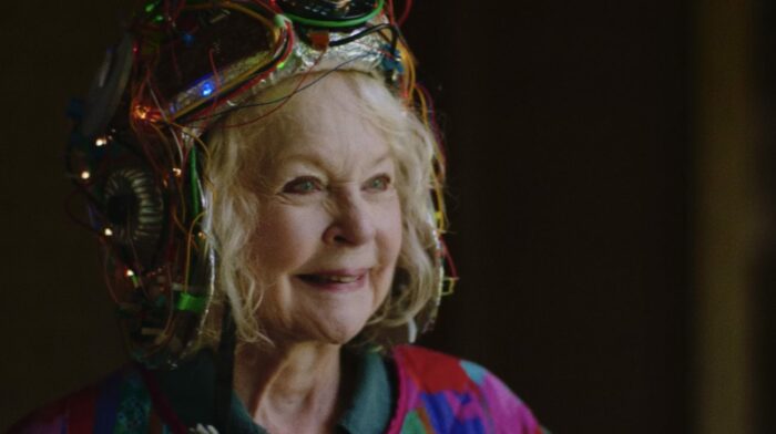 An older woman smiles while wearing an odd helmet of lights.