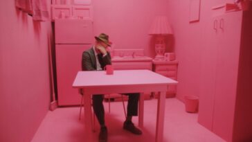 A man holds his head in confusion in a kitchen entirely painted pink.