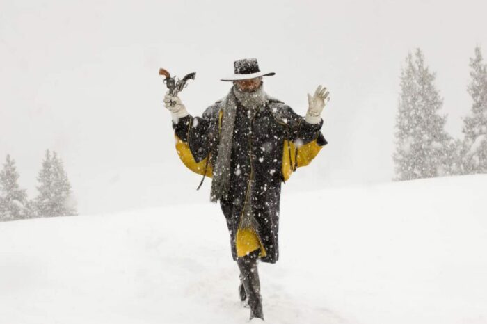 A man holds two guns and his arms in the air outside in the snow.