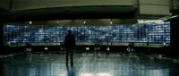 Lucius Fox (Morgan Freeman) standing in front of a wall of screens