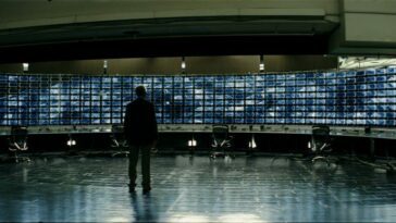 Lucius Fox (Morgan Freeman) standing in front of a wall of screens