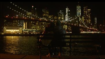 Image from In A New York Minute: A couple sits in front of the Brooklyn Bridge at nighttime.