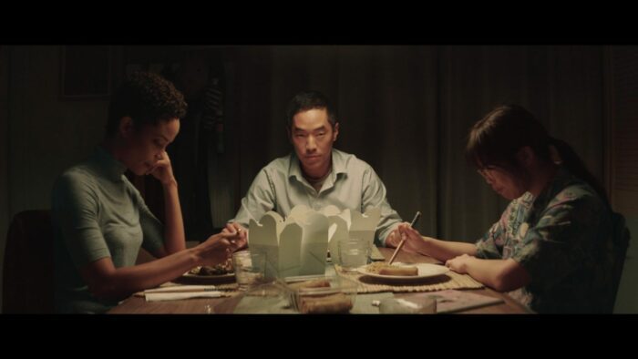 A father stares across a dinner table next to two women.