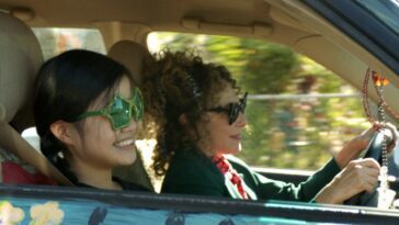 Two women in sunglasses smile while driving.