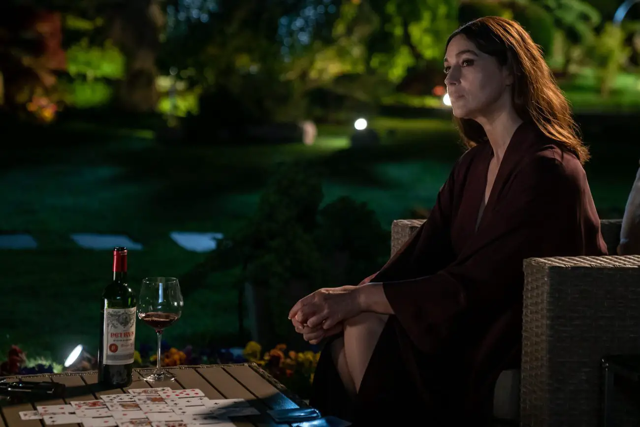 Davana Sealman (Monica Bellucci) sits with a glass of wine and game of Solitaire in her garden.
