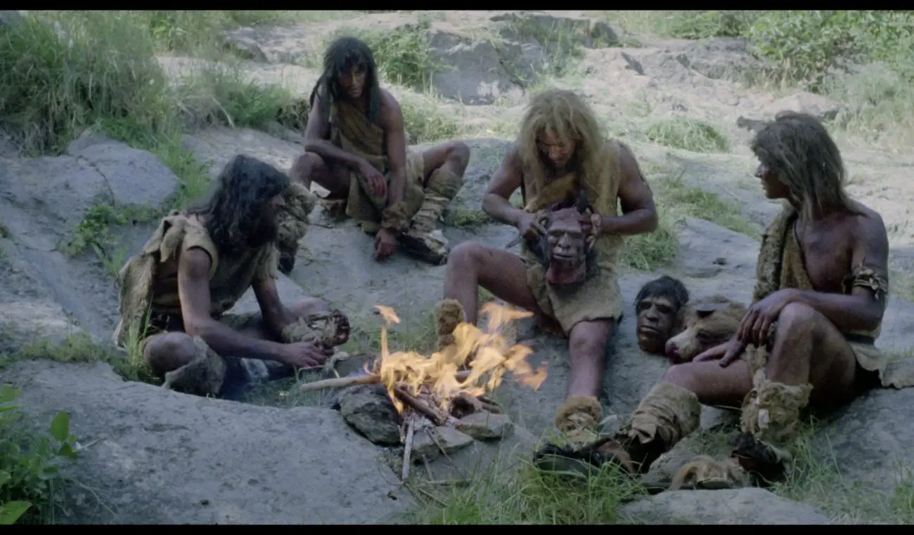 A group of cavemen sitting around a fire with decapitated heads near them