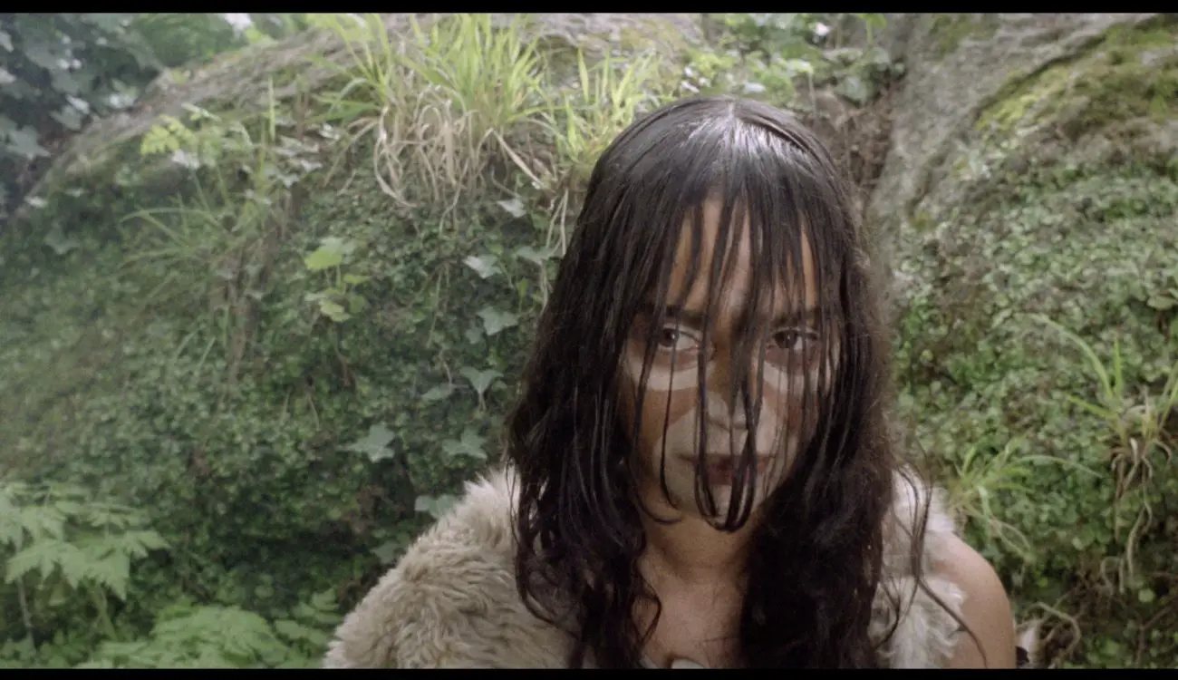 A female cavewoman looks to her right with long hair covering her face