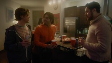Three guys talk at a kitchen counter