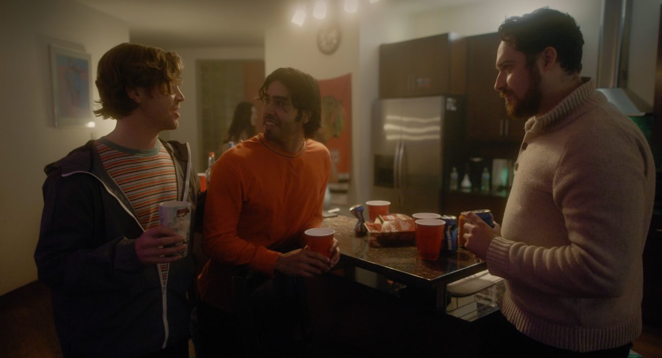 Three guys talk at a kitchen counter