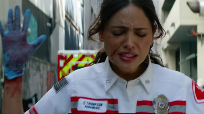 Cam (Eiza Gonzalez) stands in fear as Danny Sharp has a gun pointed at her in AMBULANCE