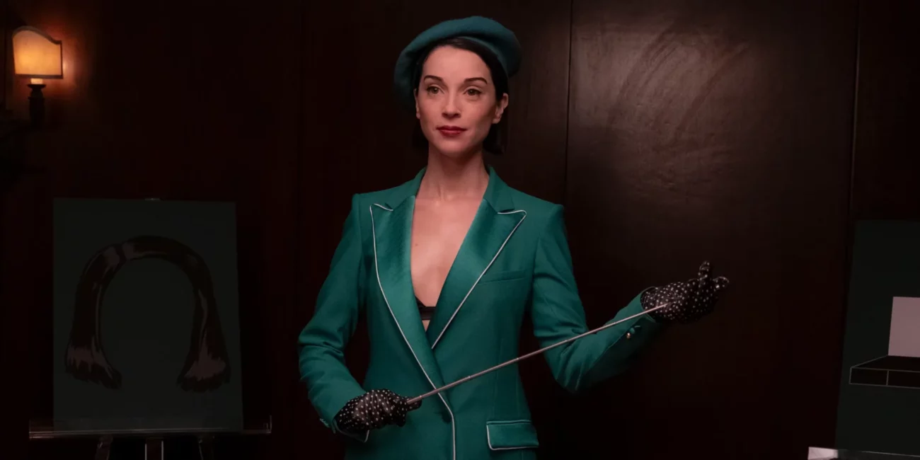 Annie Clark in a green suit holding a pointer stick