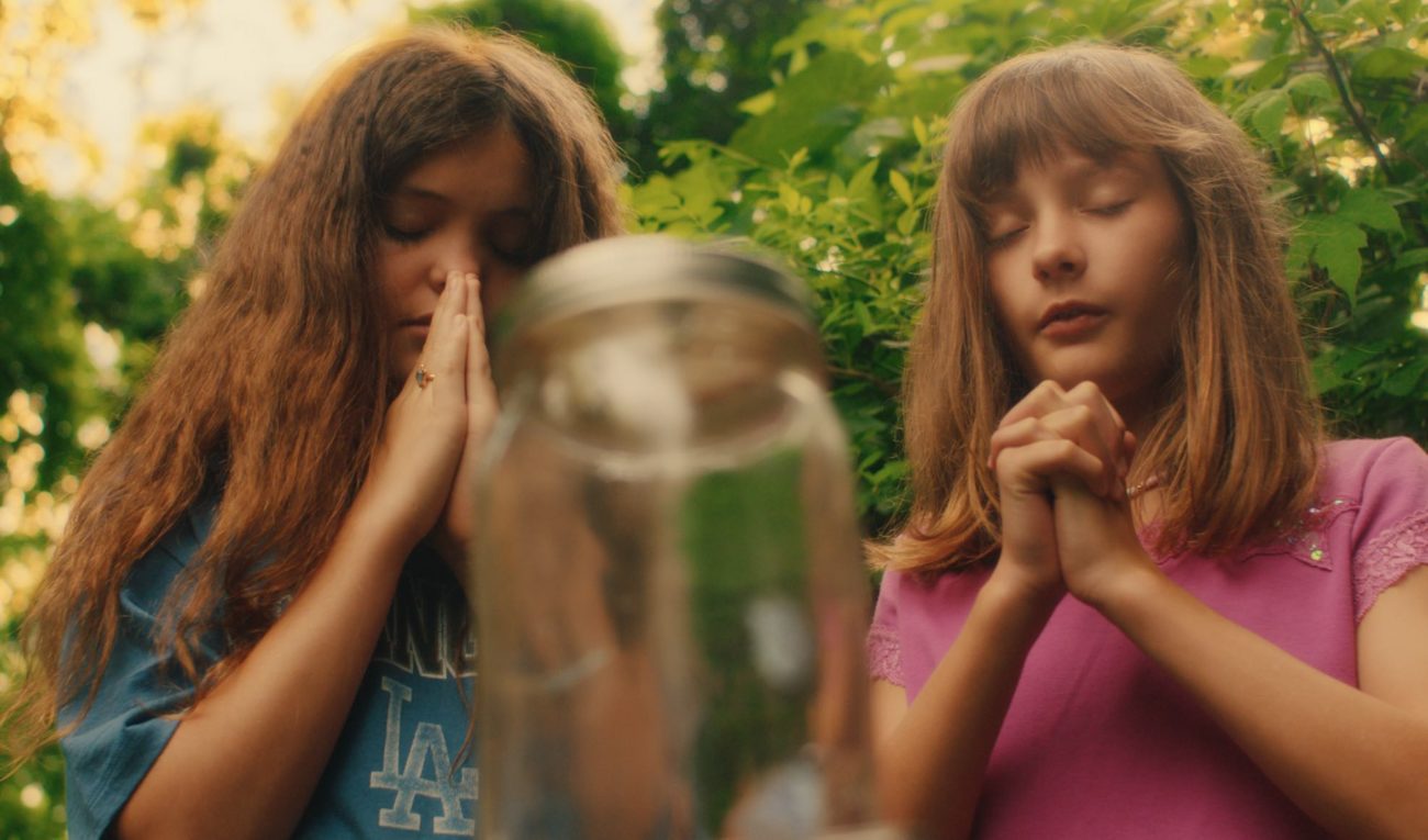 Two girls with clasped hands, praying over glass jar