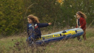 Two young girls run down a hill with an inflatable raft