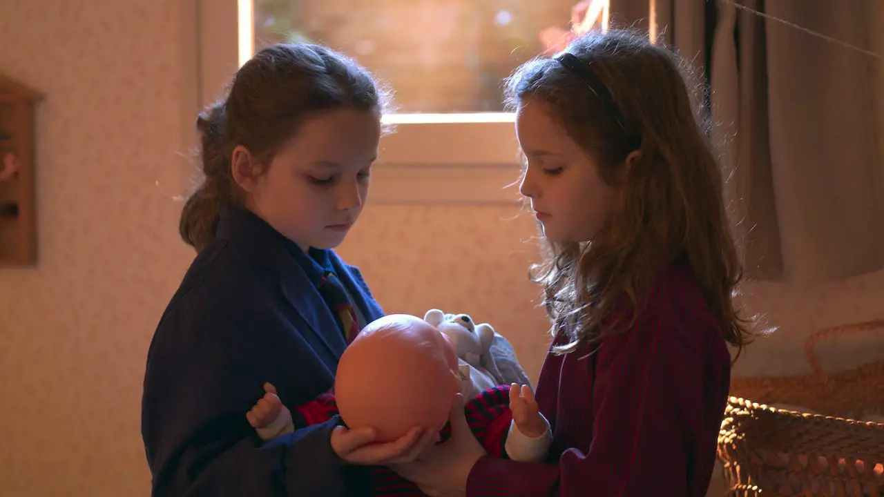 Two young girls hold a baby doll between them