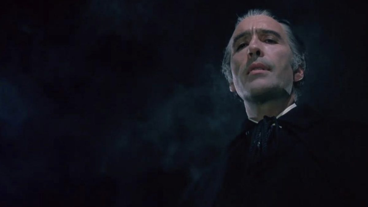 A screenshot from Dracula A.D. 1972 shows Count Dracula (Christopher Lee) sneering down at the camera from on high before a black night’s sky 