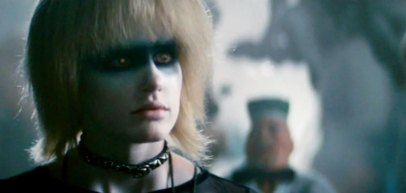 A screenshot from Blade Runner shows Pris (Daryl Hannah) made up in white face paint with a black bar of paint across her eyes, looking numbly beyond the camera