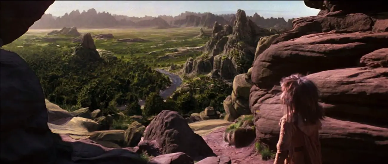 A screenshot of The Dark Crystal shows Jen, a humanoid puppet, looking out over a hill’s ridge, into the vast and undulating green hills below