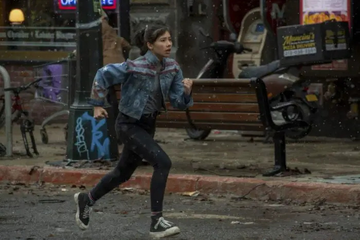 A young woman in a denim jacket runs towards trouble.