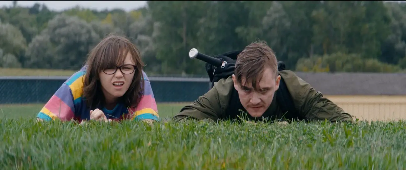 Patty (Emily Skeggs) and Simon (Kyle Gallner) lay in the grass.