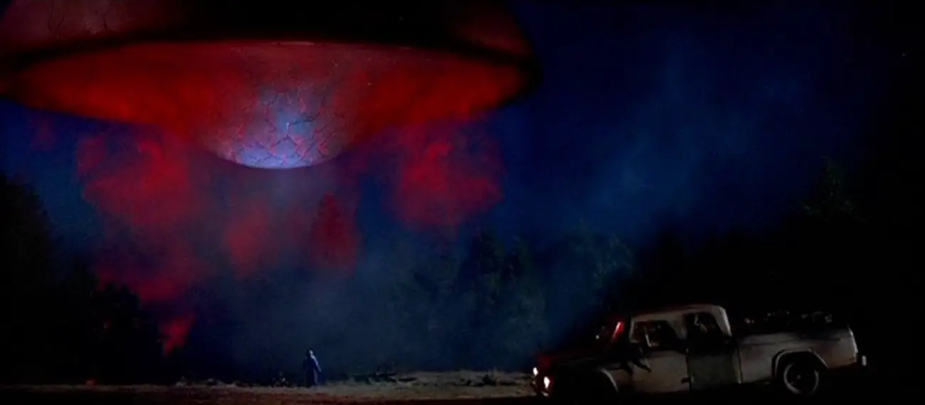 An alien ship hovers with a truck parked underneath.