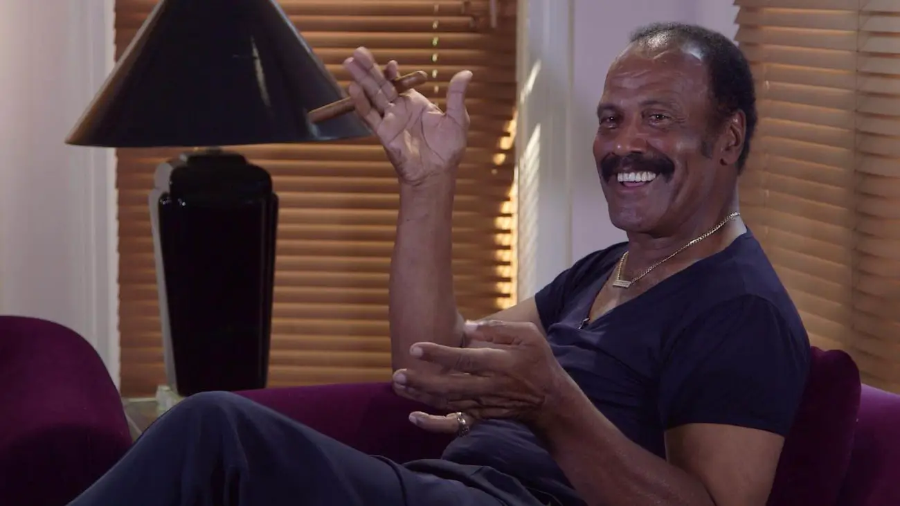 Fred "The Hammer" Williamson sitting in a chair smiling with a cigar in hand.