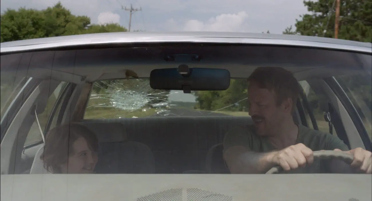 Cooper J. Friedman as Tyler and David Sullivan as Wayne in a car with a broken rear window.