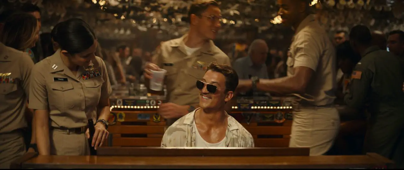 A smiling man in sunglasses plays piano at a bar.