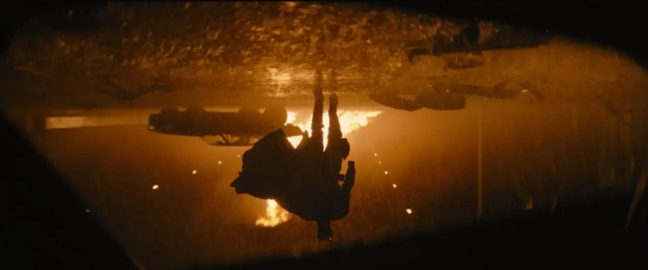 Upside-down shot of Batman in the rain with the Batmobile and fire behind him.