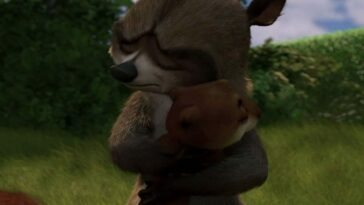 RJ, a brownish gray raccoon with white muzzle and black nose, closed eyes, hugging Hammy, a ginger squirrel, in a grassy area in front of some shrubbery.