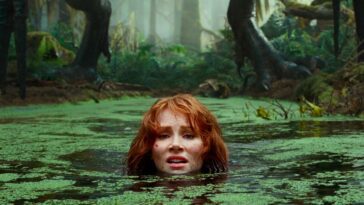 A woman lowers herself into a swamp to avoid a pursuing dinosaur.