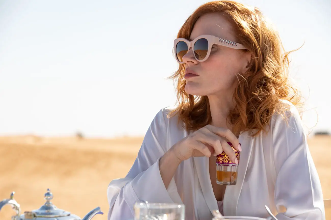 A woman in sunglasses enjoys a glass of tea outdoors.