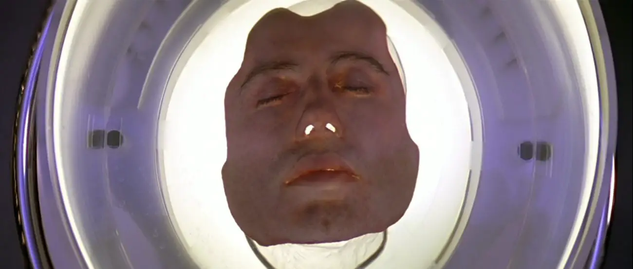 Image from Face/Off: Sean Archer's face sits in a vat of viscous fluid.
