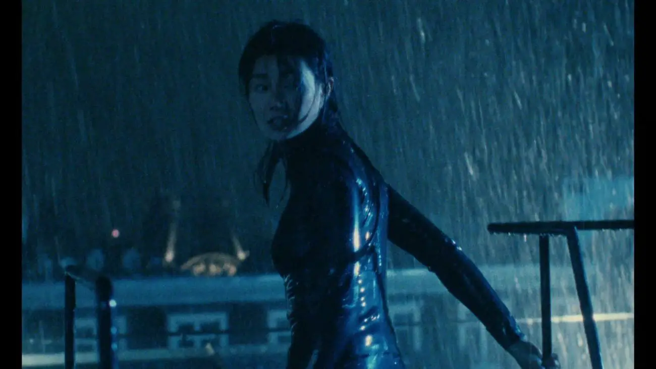 Maggie Cheung, wearing a catsuit, on a rooftop in the rain.