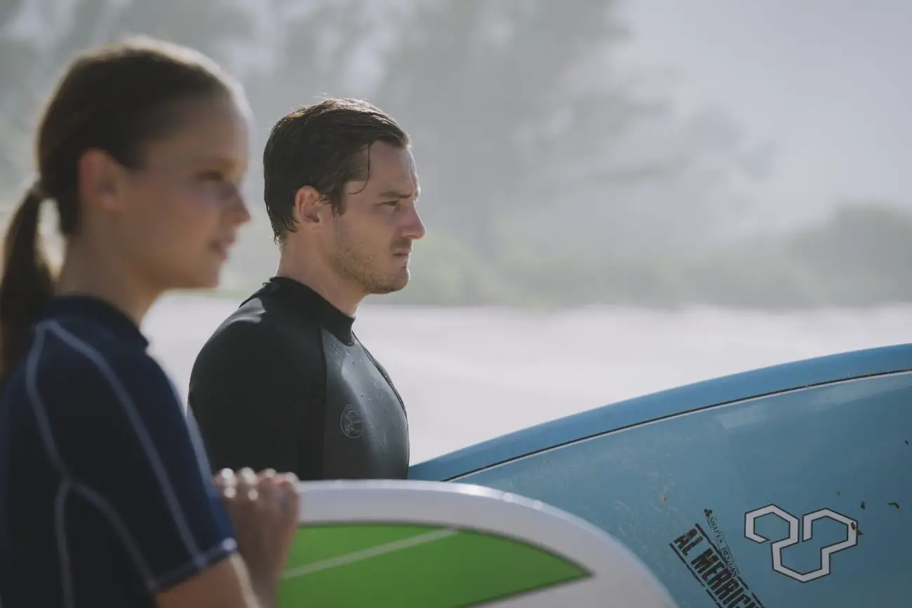 A man and woman look to the sea with surfboards under their arms.