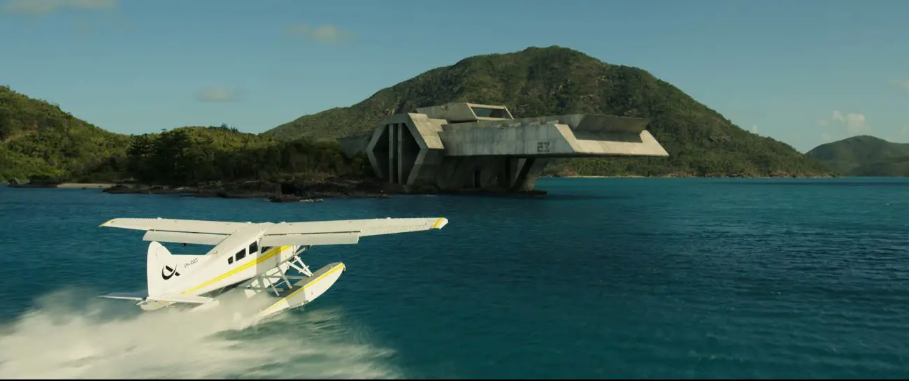 A seaplane lands near a coastal concrete facility.