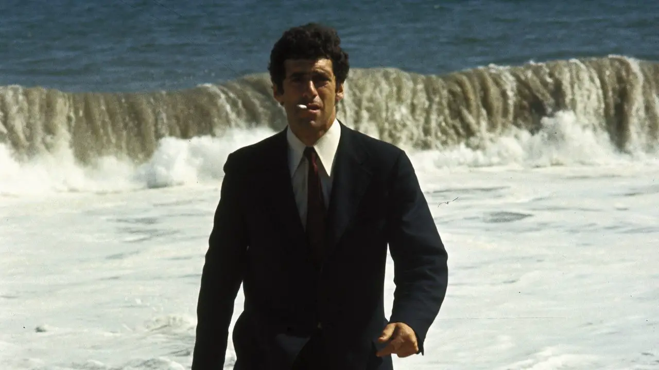 Marlowe with a cigarette in his mouth approaches with waves crashing behind him.