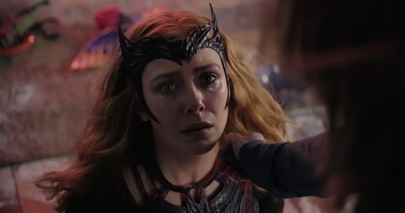 Wanda Maximoff kneeling, tears in her eyes, looking up as a hand reaches toward her face