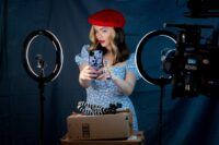 Danni in a red beret poses for a selfie in front of ring lights and a blank background