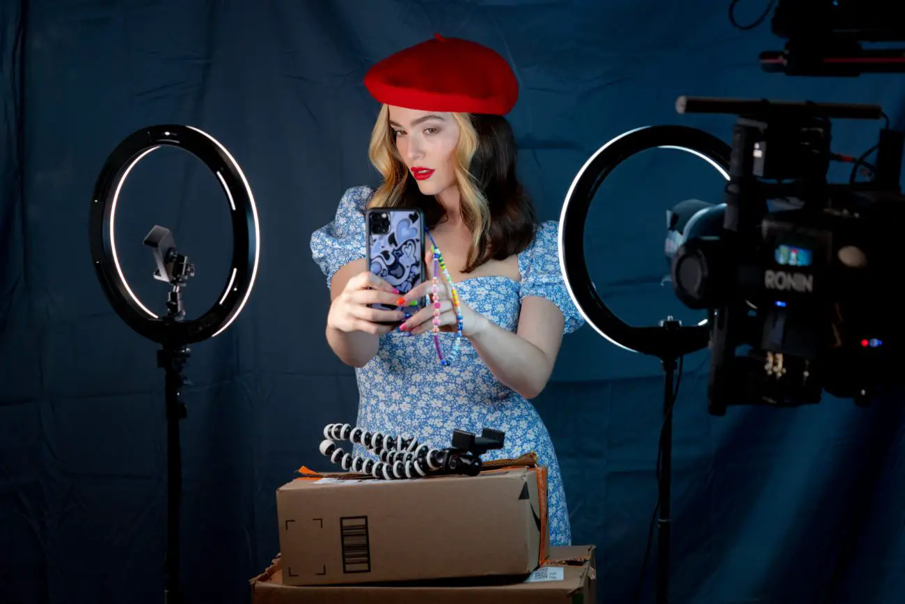 Danni in a red beret poses for a selfie in front of ring lights and a blank background