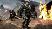 A man in an armed exo-suit looks around the battlefield scene.