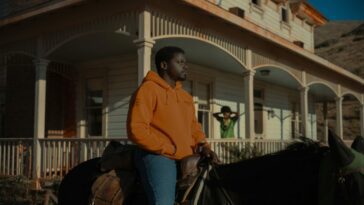 A man is mounted on a horse near a house's porch