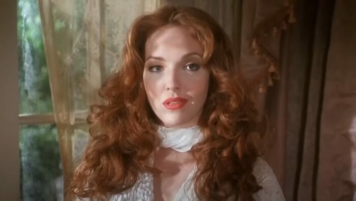 Red haired Amy Yasbeck standing at a sunlit window in Dracula: Dead and Loving It