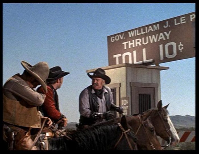 A group of cowboys outside a toll booth constructed in the middle of the desert