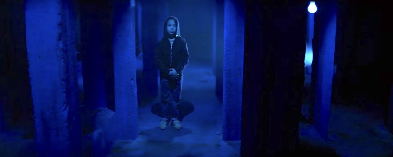 Billy standing between concrete pillars bathed in blue light.