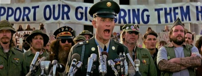 Tom Hanks as Forrest Gump in the film Forrest Gump, dressed as a Vietnam veteran speaking at a rally surrounded by other vets.