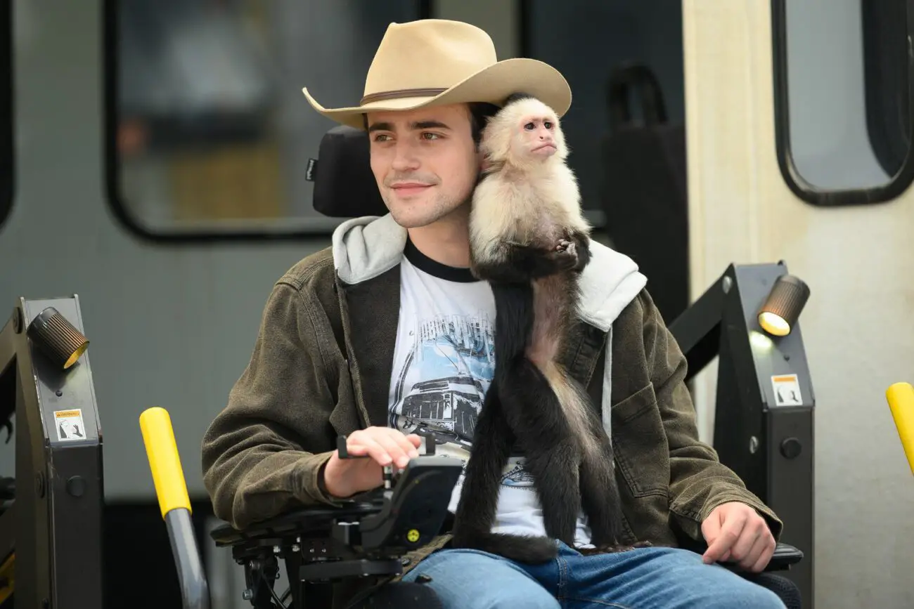 A young man in a wheel chair with a capuchin monkey.
