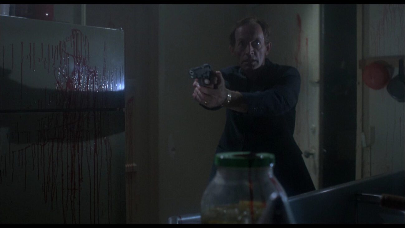 McCarthy with his gun drawn in a room with blood on the walls.