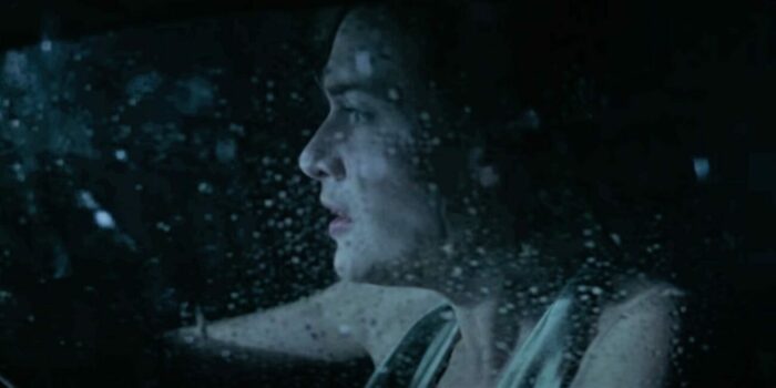 Kate Winslet in the miniseries Mildred Pierce, seen through a rain speckled car window at night.